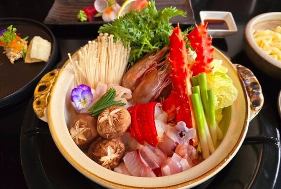 A ceramic hot pot containing raw ingredients of fish, mushrooms, spring onions, prawns and herbs.