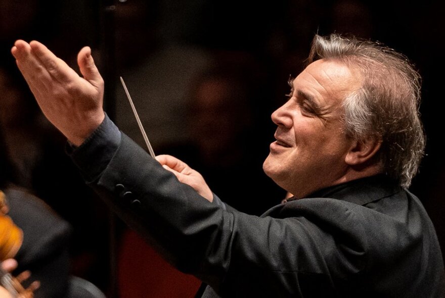 Orchestra conductor Jaime Martín in profile with one arm raised in front of him and the other hand holding his conductor's baton.