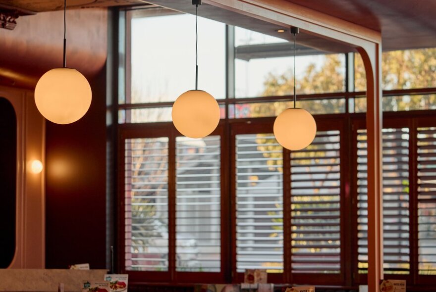 The interior of a Pancake Parlour restaurant at Docklands, showing timber plantation shutters in the window and three hanging light fittings above the dining tables.