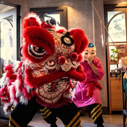 A Chinese lion dance performance taking place inside a restaurant, with several people, including children, watching.