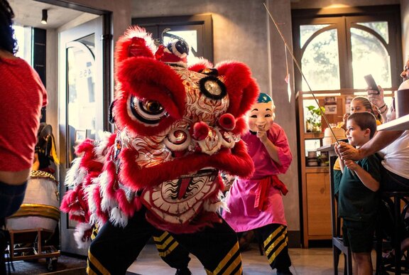 A Chinese lion dance performance taking place inside a restaurant, with several people, including children, watching.