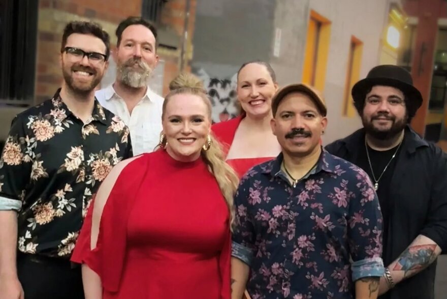 Six members of a band posing in the street for a group photo, all of them smiling.