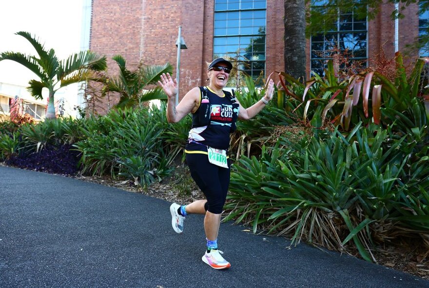 A woman smiling during a charity fun run past some vegetation and palms.