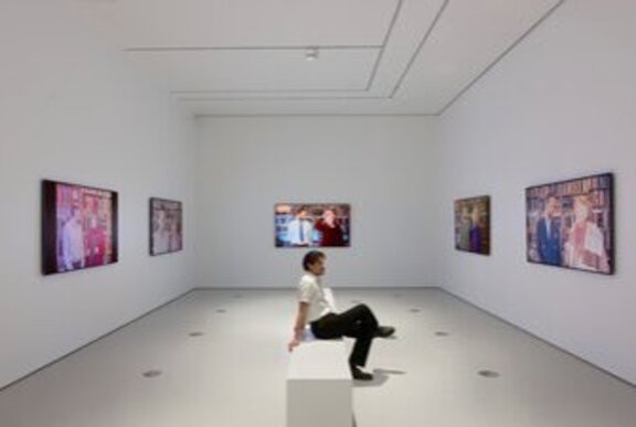 Person seated on a bench in a gallery space looking at the artworks on the walls.