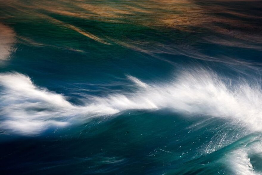 Rolling waves in the sea, with white spray at the top of one of the waves.