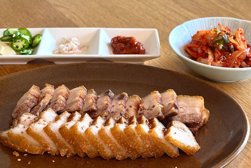 A Korean dish of sliced meat with a bowl of kimchi and condiements. 
