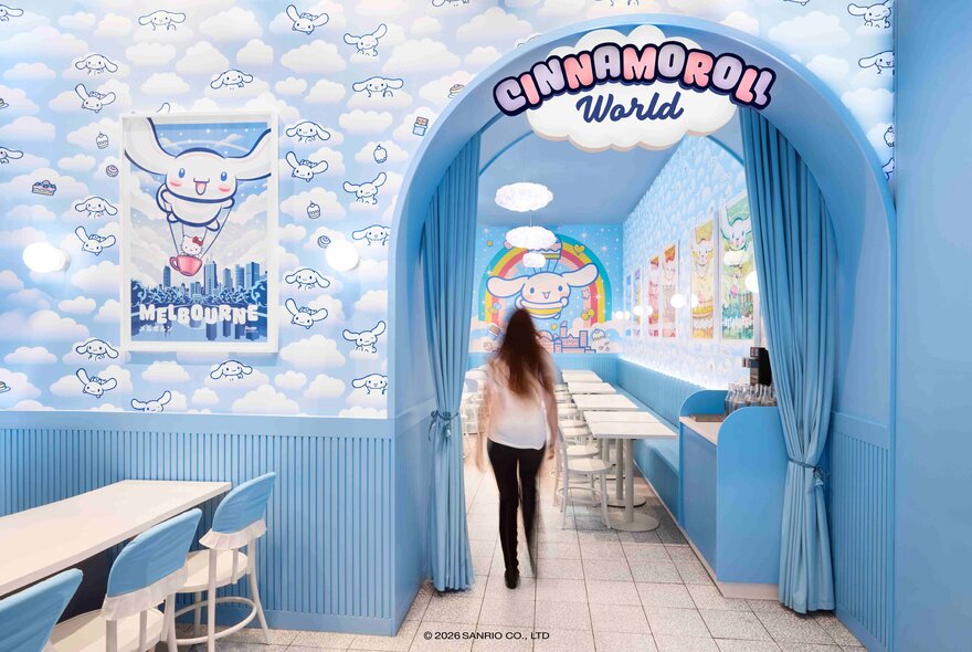 The light blue cloud-covered entrance to a blue shopfront; a woman walking into the store.
