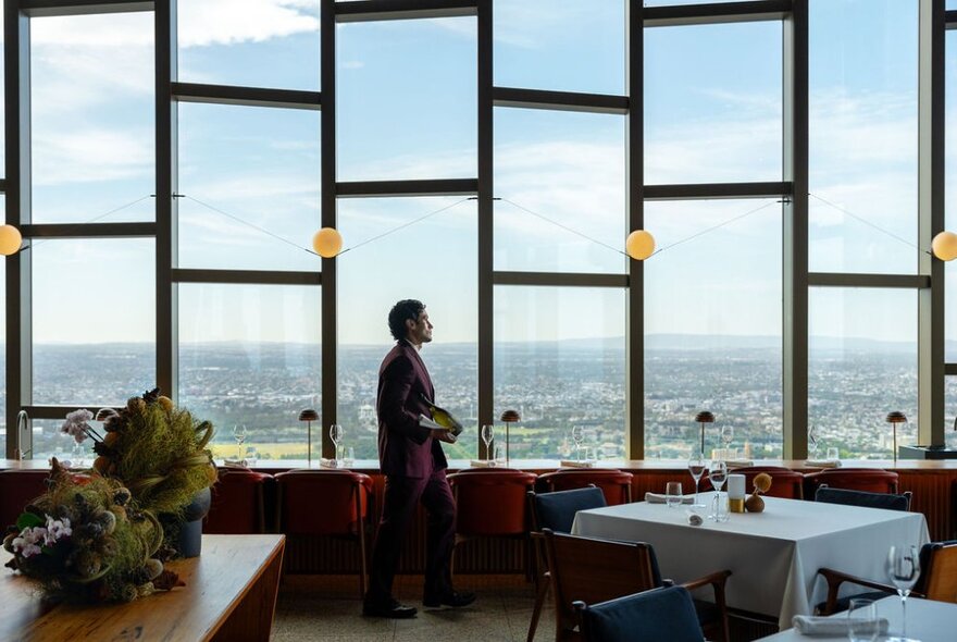 The dining room at the Ritz Carlton Hotel, with  tables placed in front of a large wall of geometric shaped windows with views over Melbourne.