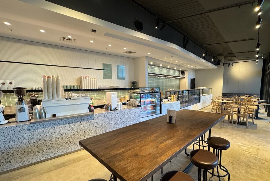 Cafe interior with table seating with stools and long serving counter with coffee machine.