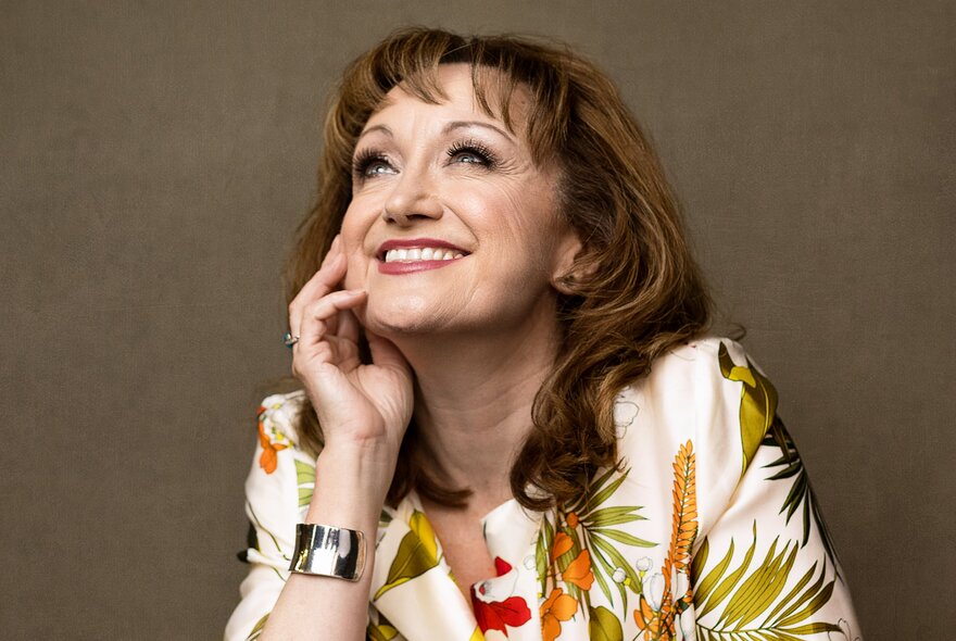 Portrait of Australian theatrical legend Caroline O’Connor AM, smiling while looking up with her hand on her cheek.
