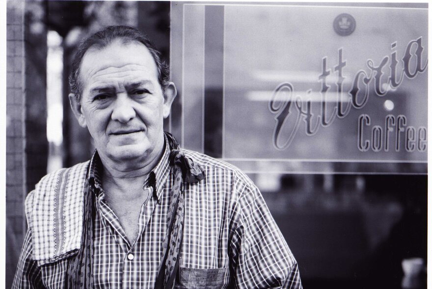 Black and white portrait photograph of Sisto Malaspina, with a tea towel over his shoulder, standing outside the front of Pellegrinis.