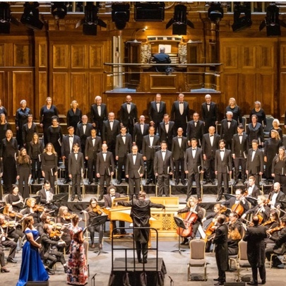 A large choir, the Royal Melbourne Philharmonic Choir standing on tiered rows behind an orchestra, performing at the historic Melbourne Town Hall.