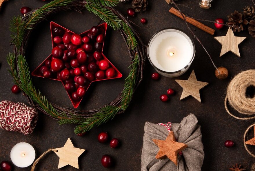 Candle surrounded by Christmas ornaments including stars, string and holly.