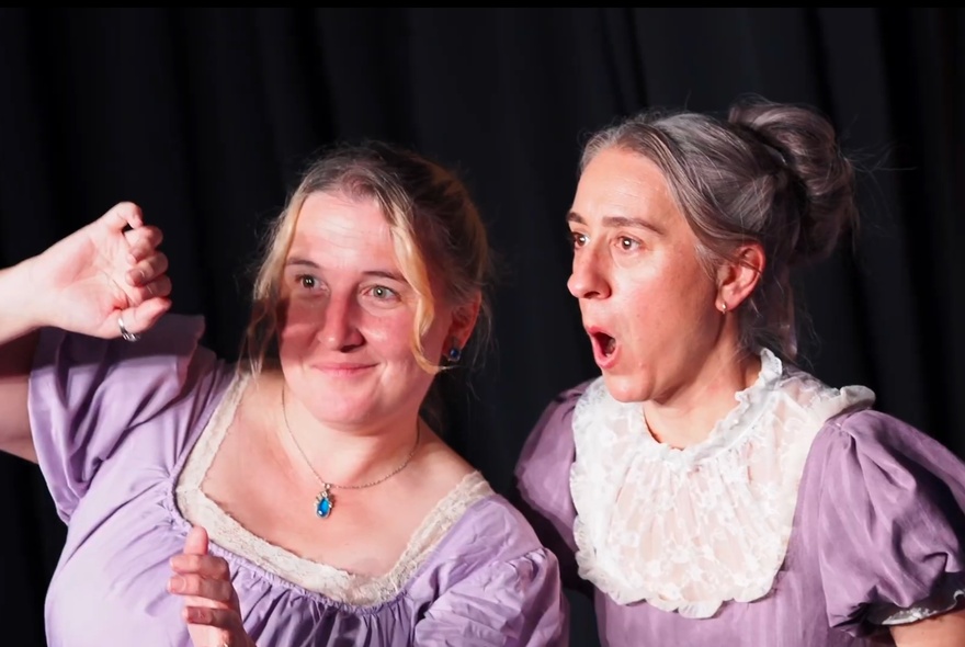 Two impro actors on stage in Regency clothing, acting out a scene.