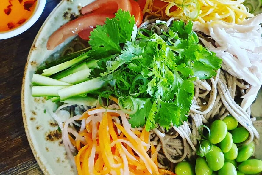 Bird's-eye close up view of a bowl of fresh vegetables, including strands of carrot, slices of zucchini and carrot, coriander atop.