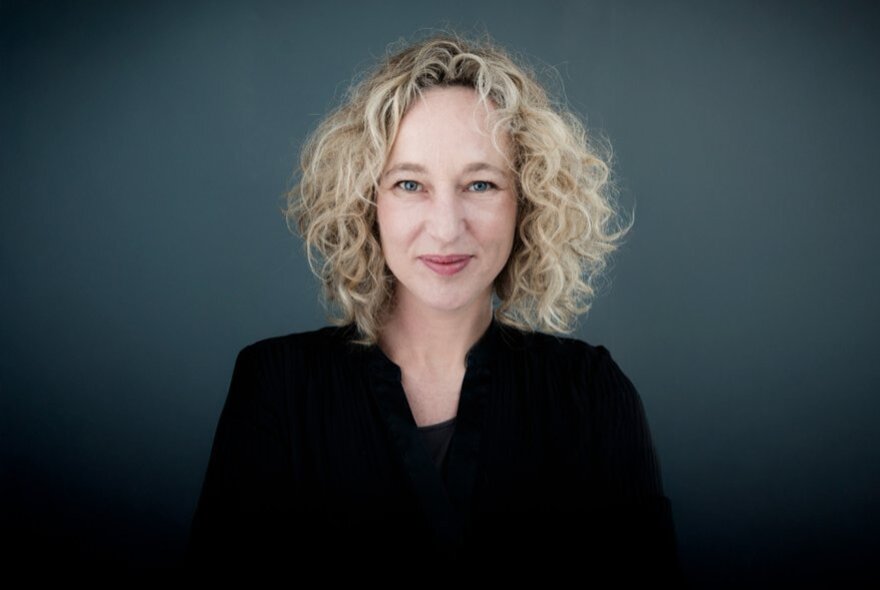 Sally Warhaft with curly blonde hair, wearing black outfit.