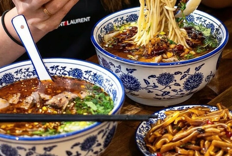 Blue floral bowls of noodles and soup with spoon and chopsticks.