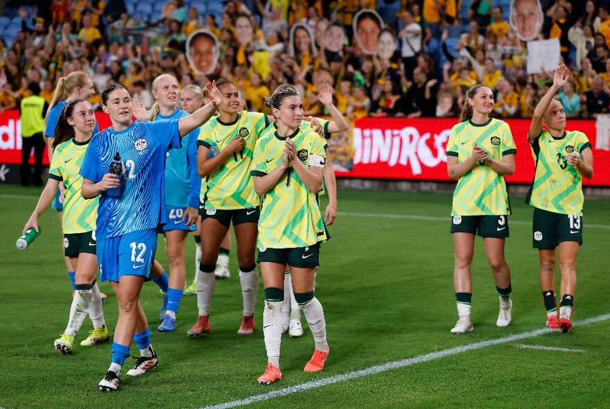 The Matildas, Australia's women's football team, walking out onto the playing pitch with a crowd of fans in the stands behind them.