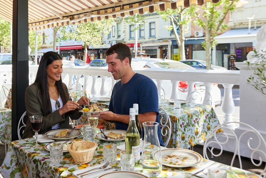 Two friends are eating Italian food outdoors at a restaurant