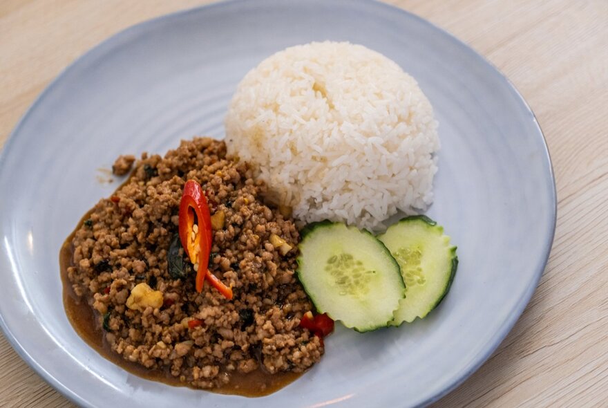 A dish of Thai meat and rice on a blue plate.