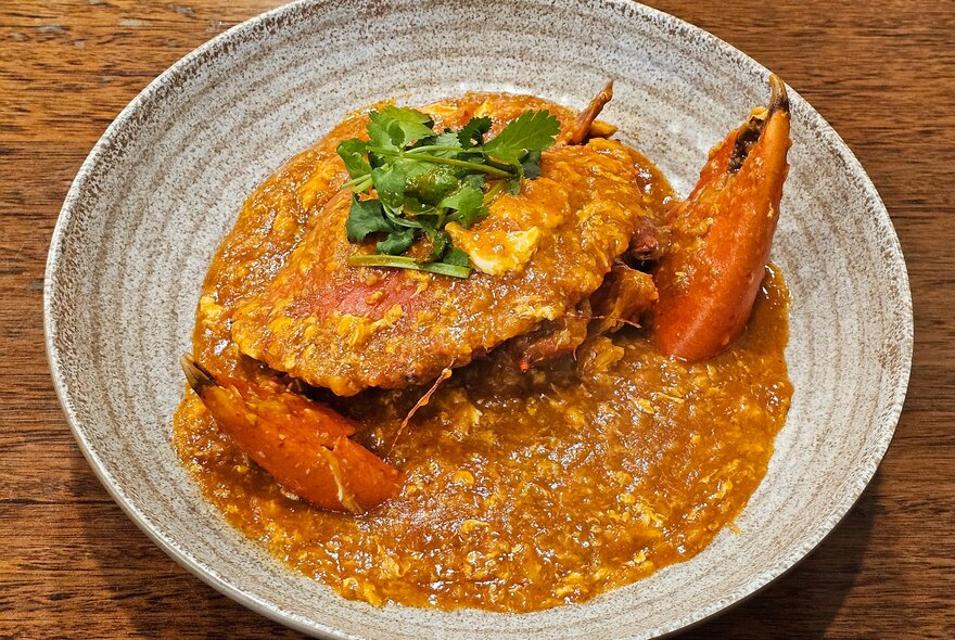 A whole fried crab in a bowl with a curry sauce and a green leafy garnish on top.