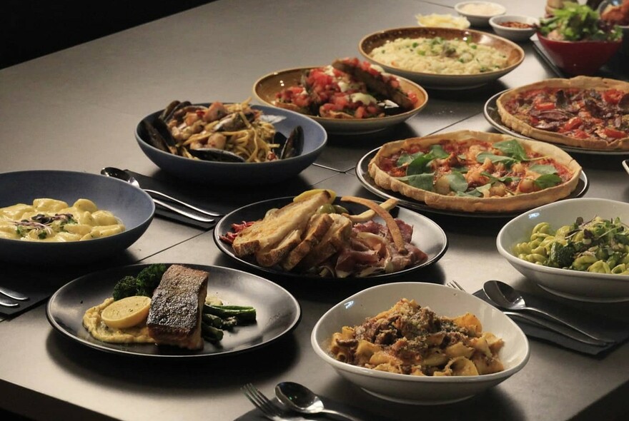 Table laid with dishes of food including pizza, gnocchi, pasta and risotto.