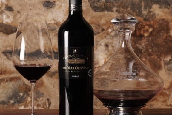 A bottle of red wine and two glasses poured against a stone background.