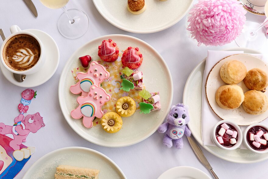 Care Bears themed high tea treats, including bear-shaped cookies with pink icing alongside cups of tea and juice.