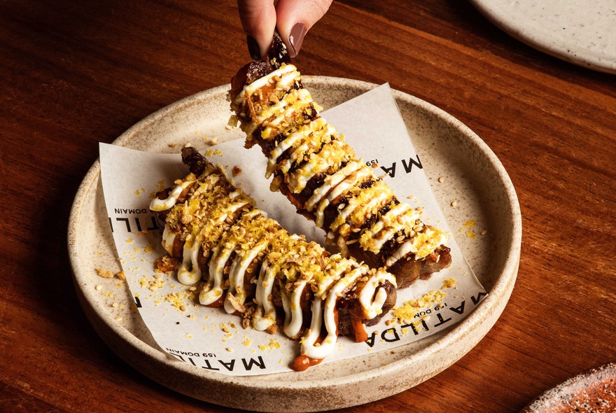 A plate showing two portions of smoked saltbush lamb ribs garnished with tahini yoghurt. 