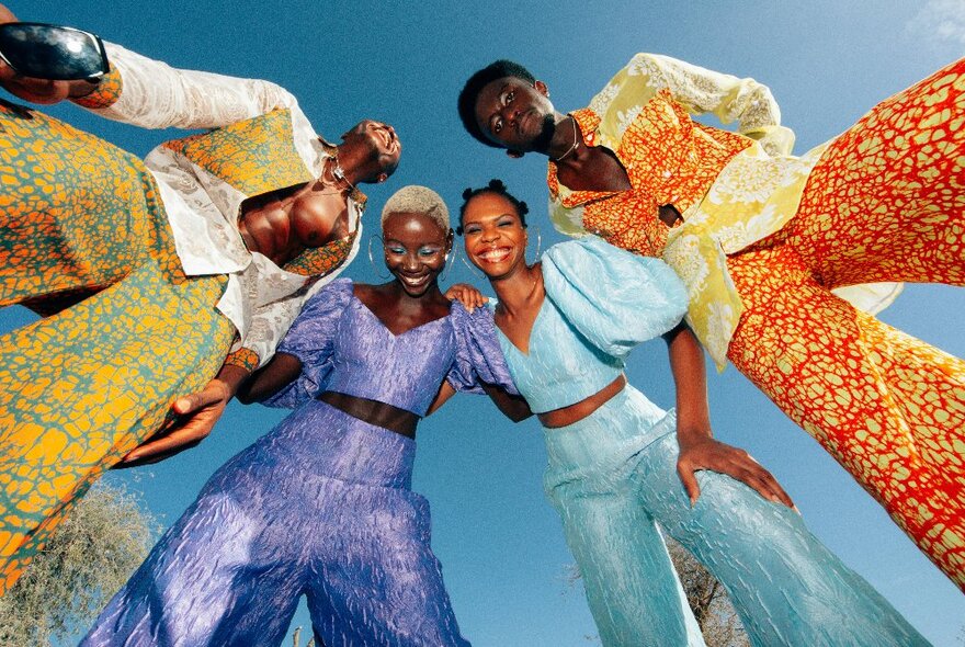 Four models dressed in bright clothes huddle in together for a photo taken from the ground up.