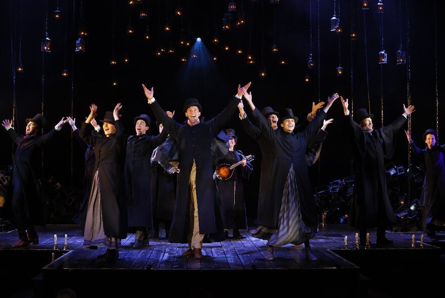 Dancers on stage in Edwardian-era costumes with a starry night sky set design.