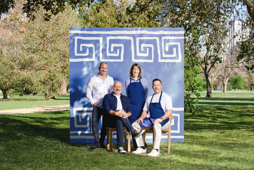 Four people in front of a Greek-themed blue and white backdrop in a garden setting.