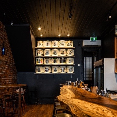 Interior of a Japanese sake bar with a rawedge timber bench and sake barrels on a shelf.