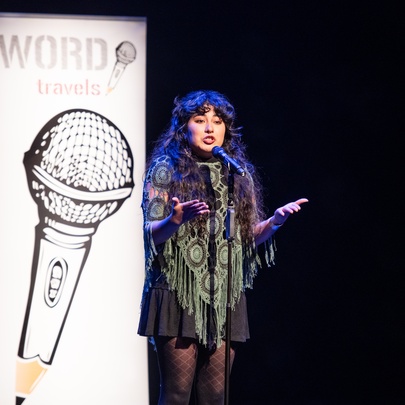 Performer on stage at a microphone, with a poster with the image of a microphone behind her.