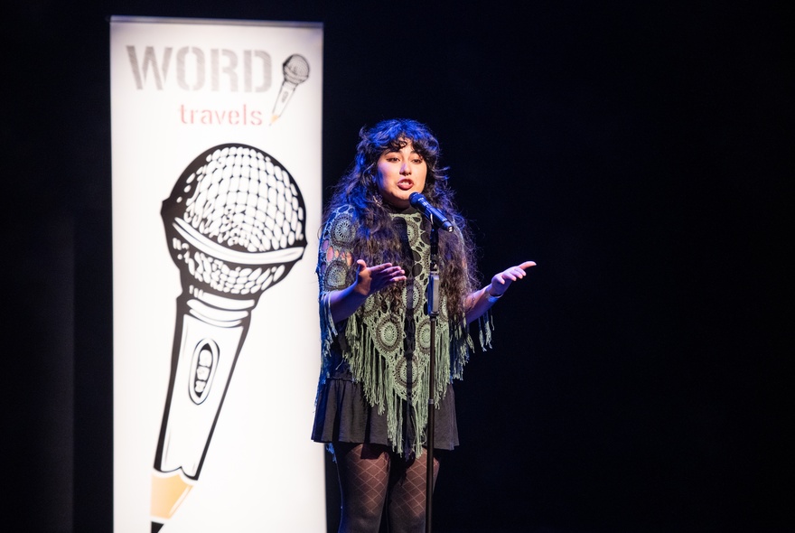 Performer on stage at a microphone, with a poster with the image of a microphone behind her.