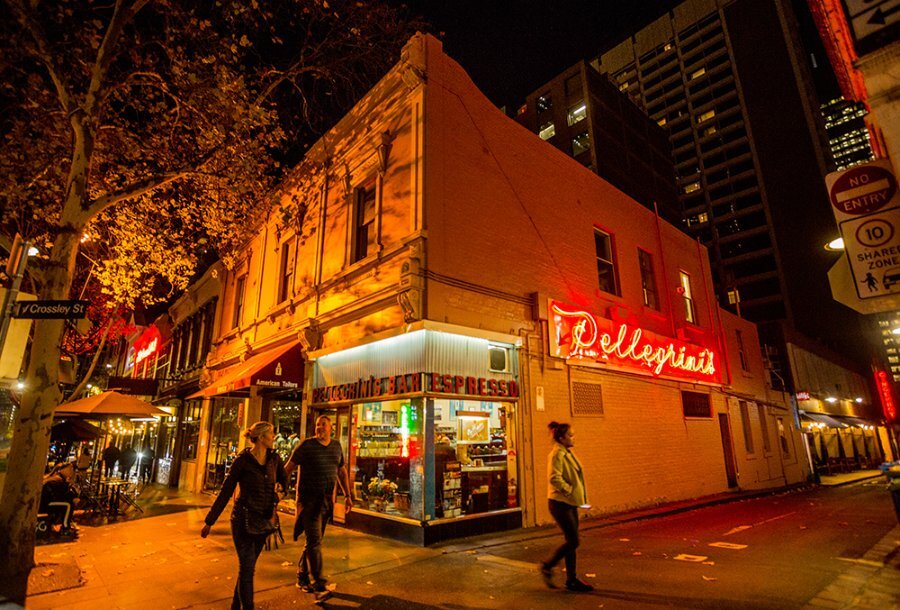People walking past a cafe with a neon red sign at night.
