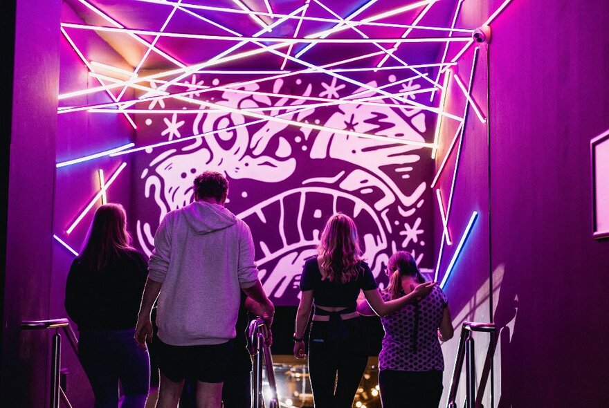 A group of four people at a bright venue with laser lights and a mural.