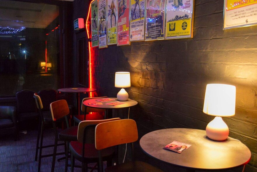 Lamplit tables in a dimly lit bar with posters on the wall.