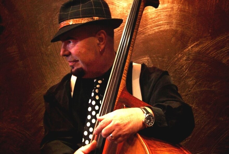 A man in a hat wearing a polka dot tie holding a double bass.