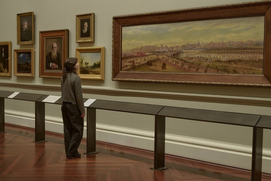 A single person looking at paintings on a wall in a gallery. 