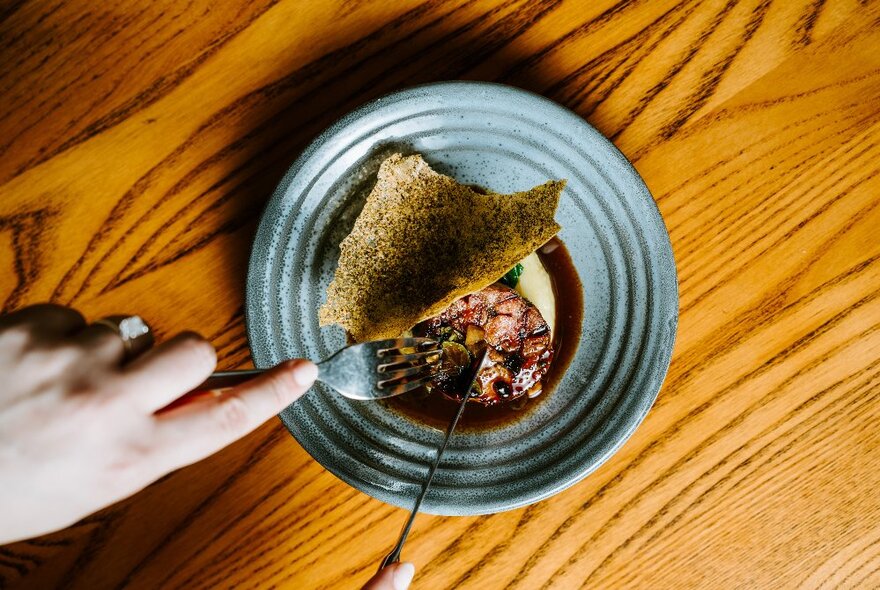 A hand using a knife and fork to cut up food on a plate.