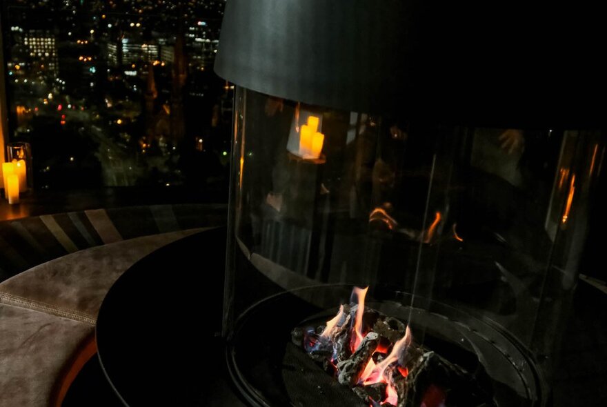 A glass enclosed fire on a round coffee table in the lounge on Sofitel's 35th floor, with nighttime city views behind.