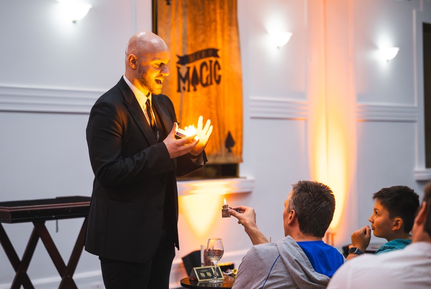 A magician performing in front of a live audience, light illuminating from his hands as if from a candle.