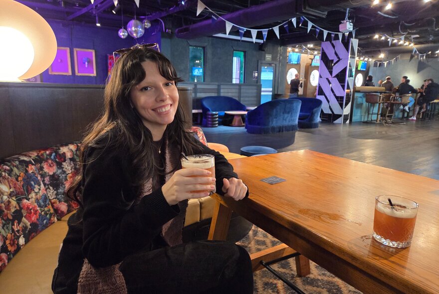 Smiling woman holding a cocktail in a large indoor space.