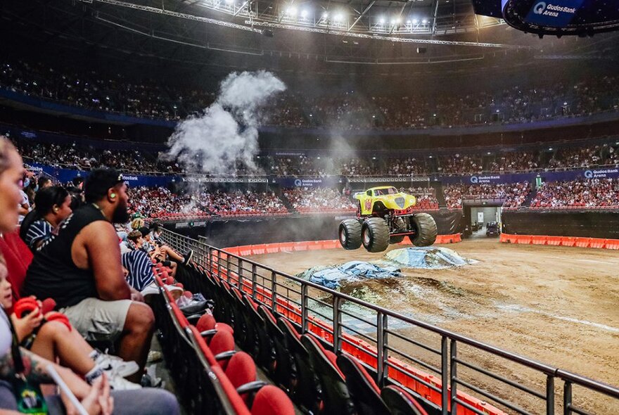 Audience looking at a monster truck in an arena on a dirt road.