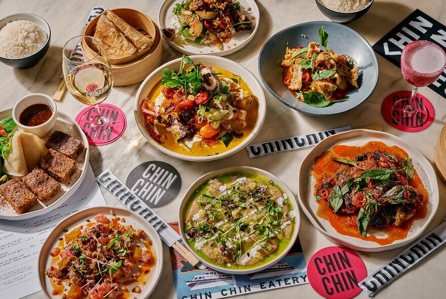 A mixed selection of bowls of Asian curries, bread and rice on a table, and glasses of wine, seen from above.