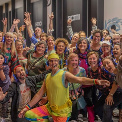 Group of people wearing headphones and posing with their arms raised in the air above their heads in a dance-style move, in front of ACMI cinema in Melbourne city.