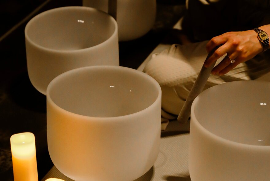 Person seated next to three white porcelain bowls and a lit candle.