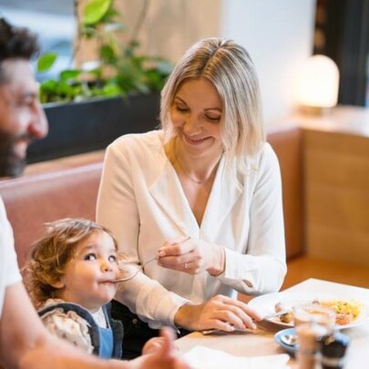 Couple seated at a table, the woman feeding a child with a fork.