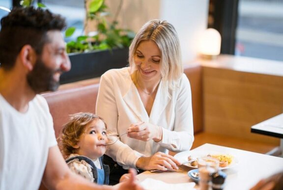 Couple seated at a table, the woman feeding a child with a fork.